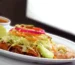 Enchiladas in red sauce topped with lettuce, onion and lime on a white platter, similar to these ground beef enchiladas