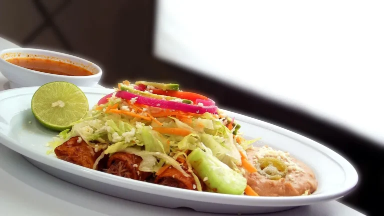 Enchiladas in red sauce topped with lettuce, onion and lime on a white platter, similar to these ground beef enchiladas