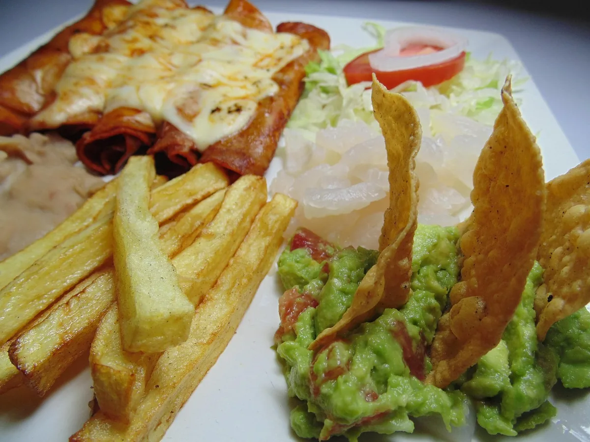 Baked enchiladas with melted cheese served with guacamole, tortilla chips and fries