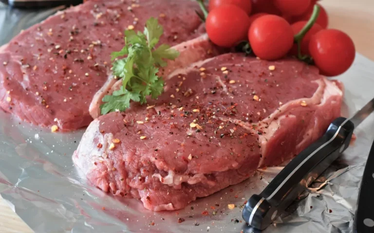 Raw beef steaks seasoned with pepper and herbs on foil, ready for a steak marinade
