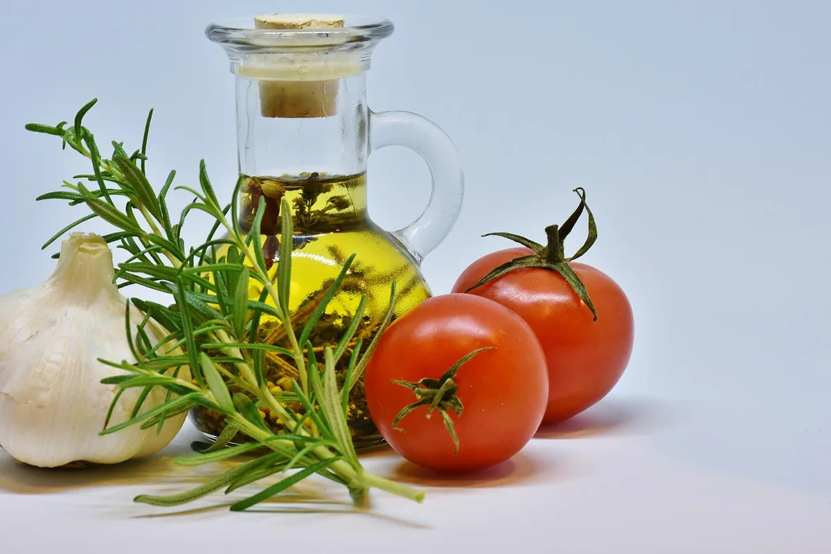 Olive oil in a glass jug with garlic, rosemary and tomatoes for an olive oil steak marinade