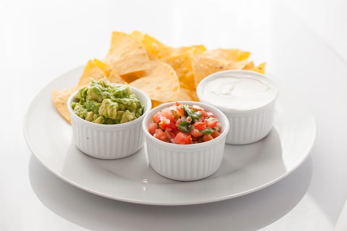 Tortilla chips with small bowls of dips for a party appetizer spread