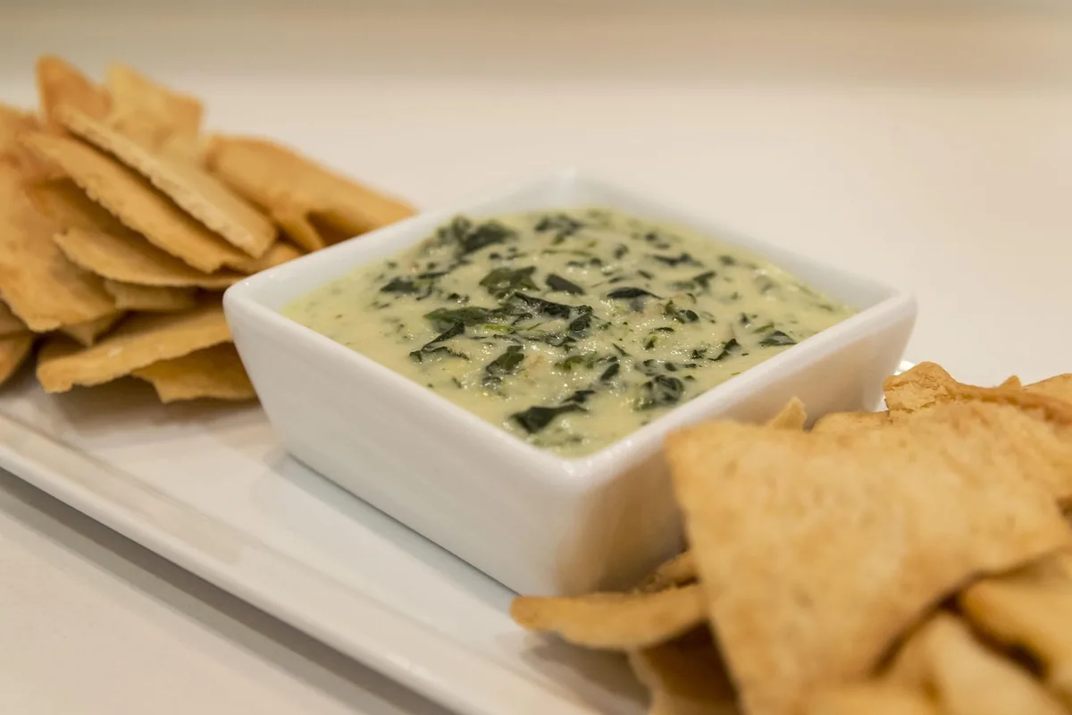 A warm baked cheesy dip in a white dish with tortilla chips, similar in texture to buffalo chicken dip