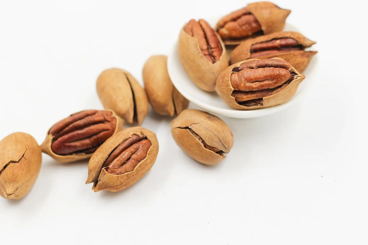 Cracked pecans in their shells in a small white bowl, the nut used in a turtle cheesecake