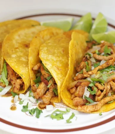 Four shredded chicken tacos in corn tortillas with cilantro and lime wedges, similar to these crockpot chicken tacos