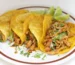 Four shredded chicken tacos in corn tortillas with cilantro and lime wedges, similar to these crockpot chicken tacos