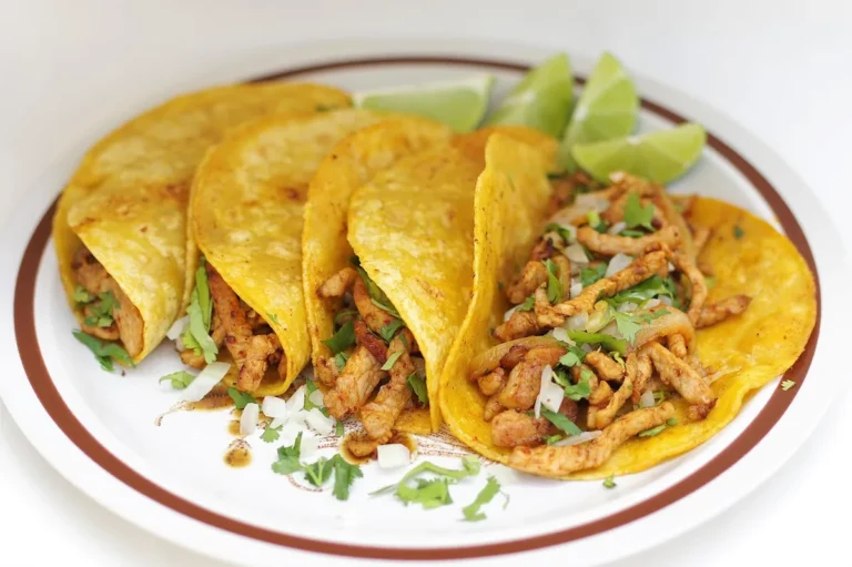 Four shredded chicken tacos in corn tortillas with cilantro and lime wedges, similar to these crockpot chicken tacos