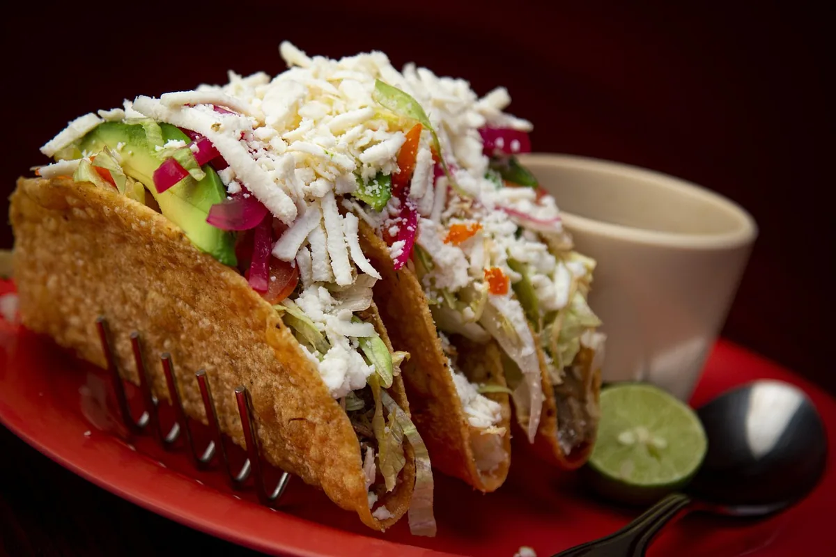 Hard shell tacos topped with shredded cheese, lettuce and avocado, a topping idea for shredded chicken tacos