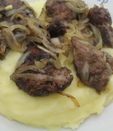 Beef liver and onions served over mashed potatoes on a blue and white plate