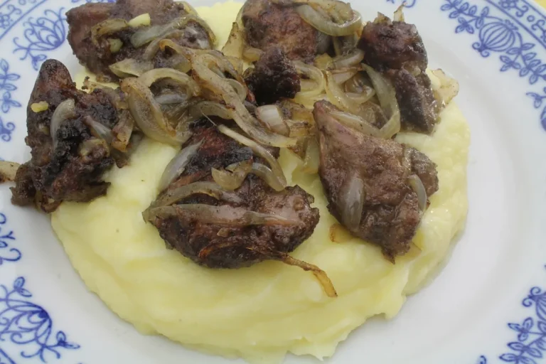 Beef liver and onions served over mashed potatoes on a blue and white plate