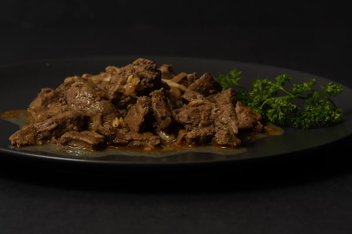 Pan-fried liver strips with onions and parsley on a dark plate, similar to beef liver and onions