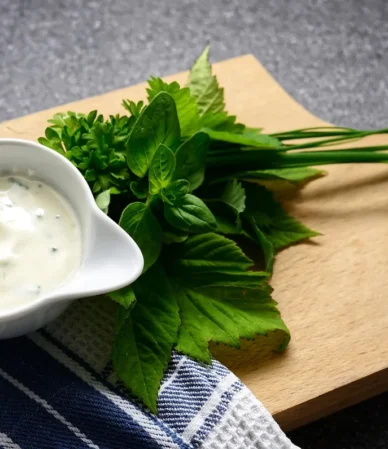 Creamy herb sauce in a white bowl with fresh herbs on a wooden board, similar to this crab cake sauce