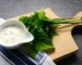 Creamy herb sauce in a white bowl with fresh herbs on a wooden board, similar to this crab cake sauce