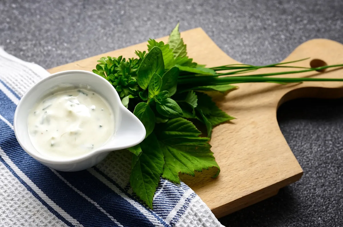 Creamy herb sauce in a white bowl with fresh herbs on a wooden board, similar to this crab cake sauce