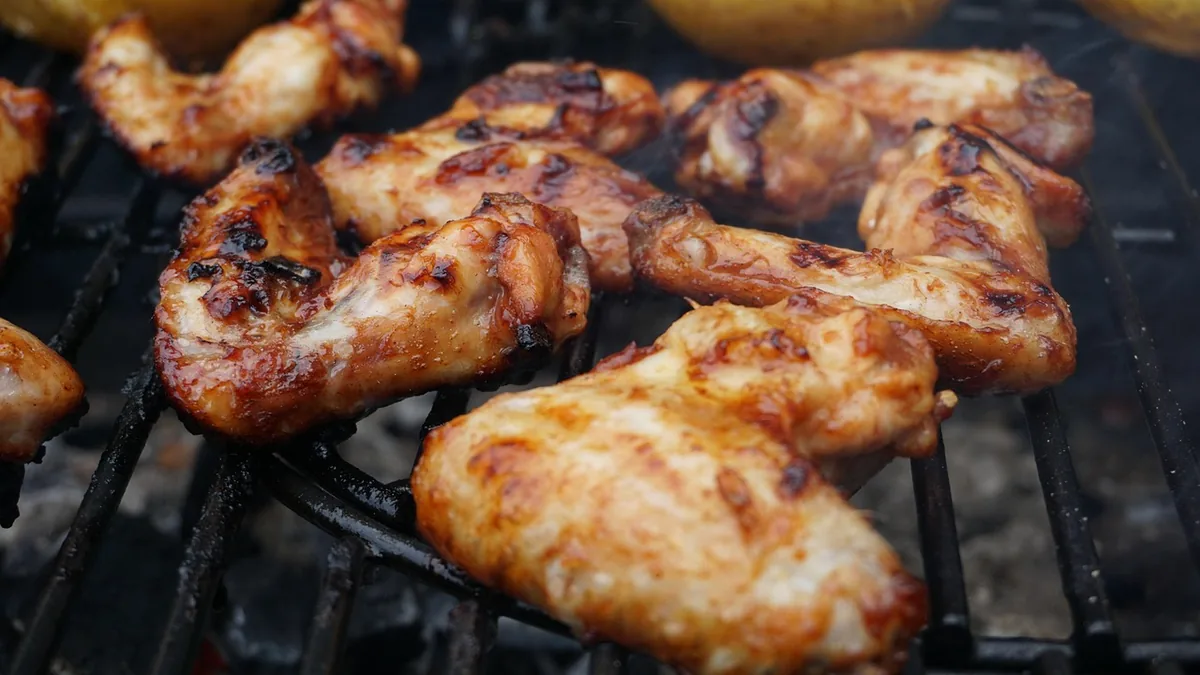 Seasoned chicken wings cooking on a grill, a grilled version of the chicken wing spice rub