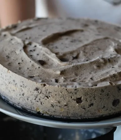 Round cake covered in speckled cookies and cream frosting on a white plate, similar to this cookies and cream cake
