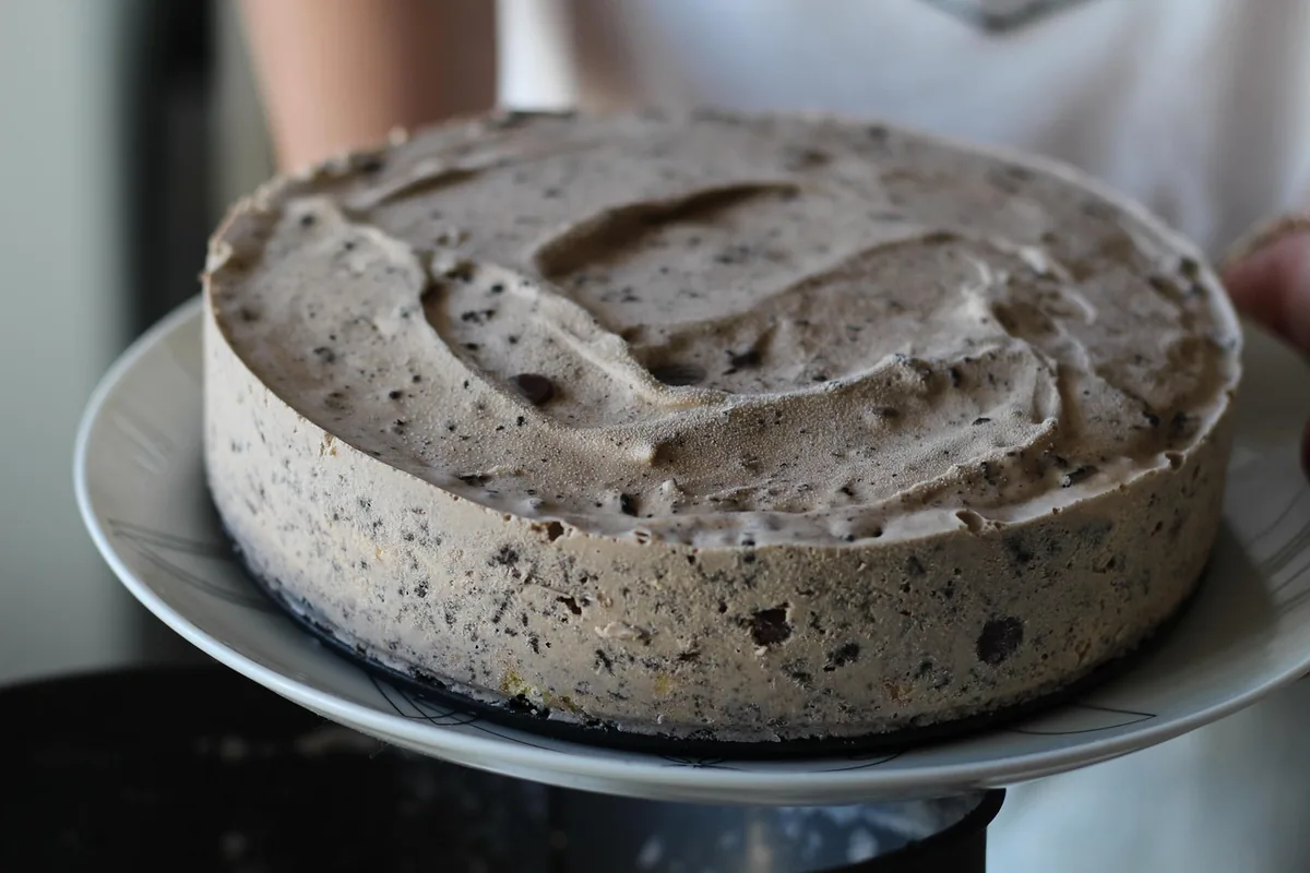 Round cake covered in speckled cookies and cream frosting on a white plate, similar to this cookies and cream cake