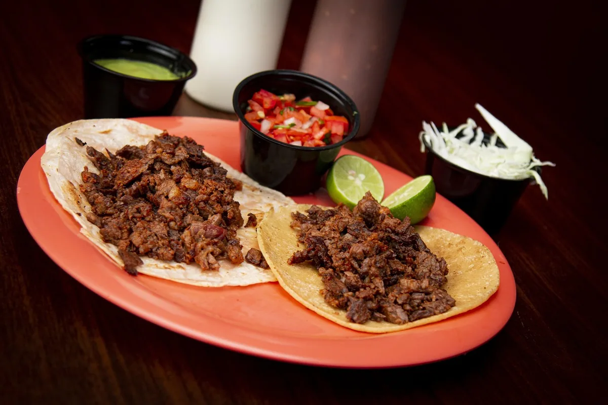 Two shredded beef tacos on corn tortillas with salsa and lime, a way to serve shredded beef