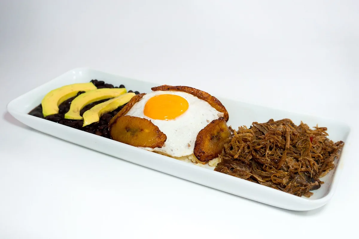 Shredded beef served on a platter with black beans, fried plantains, avocado and a fried egg