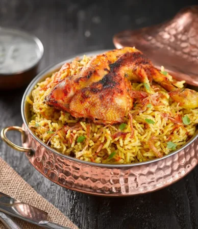 Spiced chicken on golden yellow rice in a copper pan with a bowl of white sauce, like halal cart chicken over rice