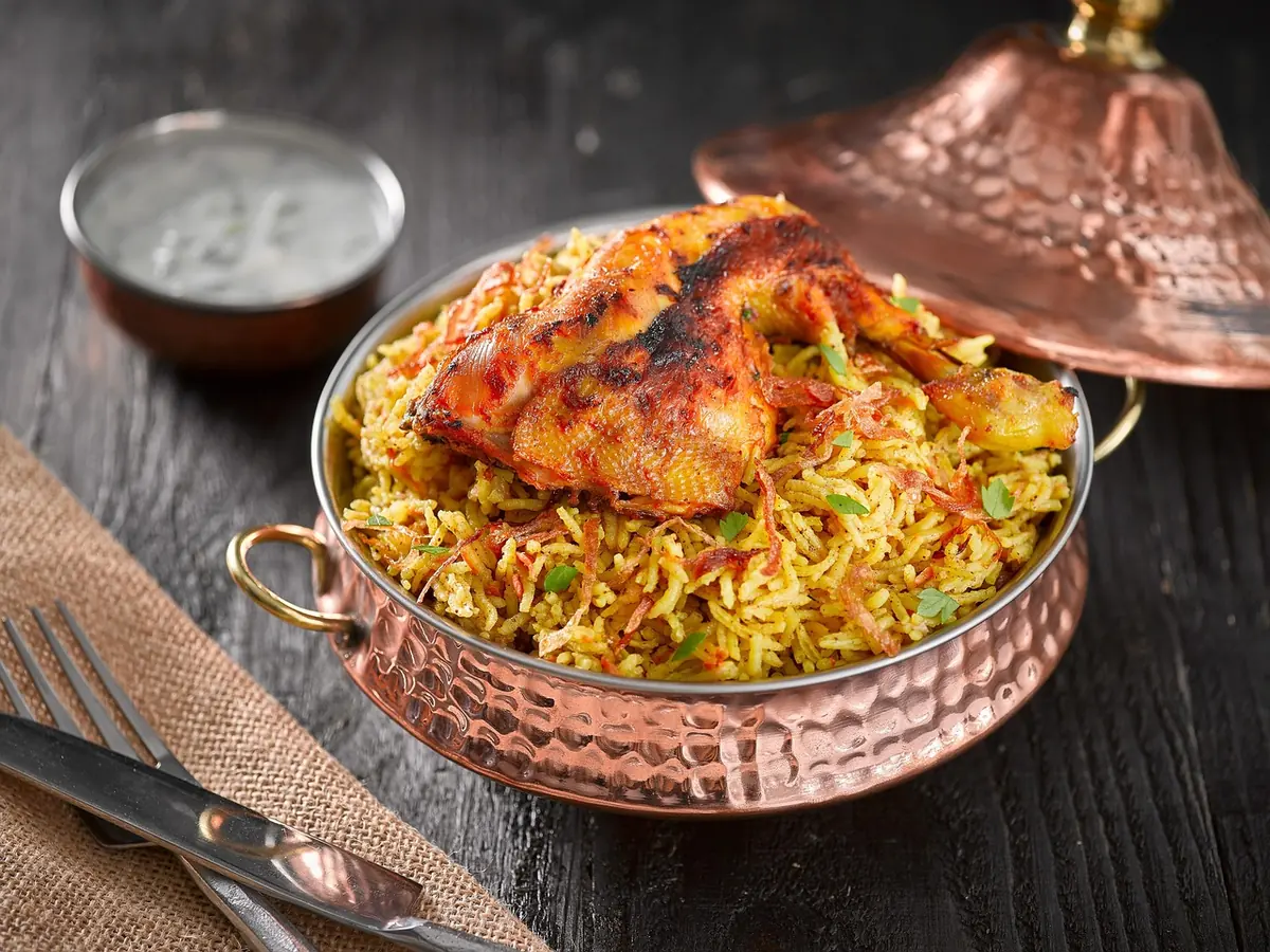 Spiced chicken on golden yellow rice in a copper pan with a bowl of white sauce, like halal cart chicken over rice