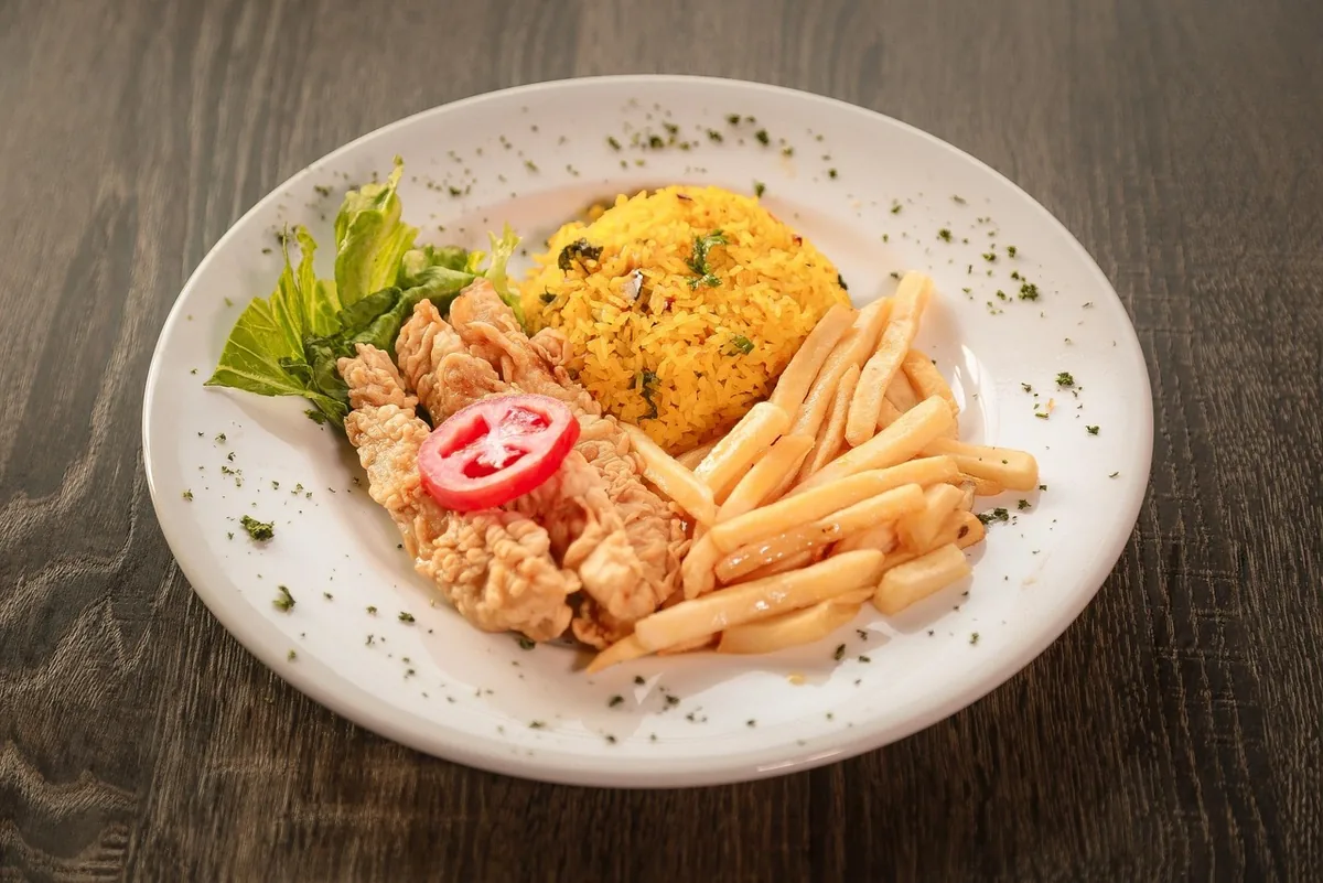 Chicken with a mound of yellow rice, lettuce and tomato on a white plate