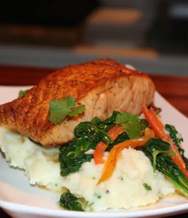 Golden baked salmon fillet on mashed potatoes with sautéed spinach and peppers, served like stuffed salmon
