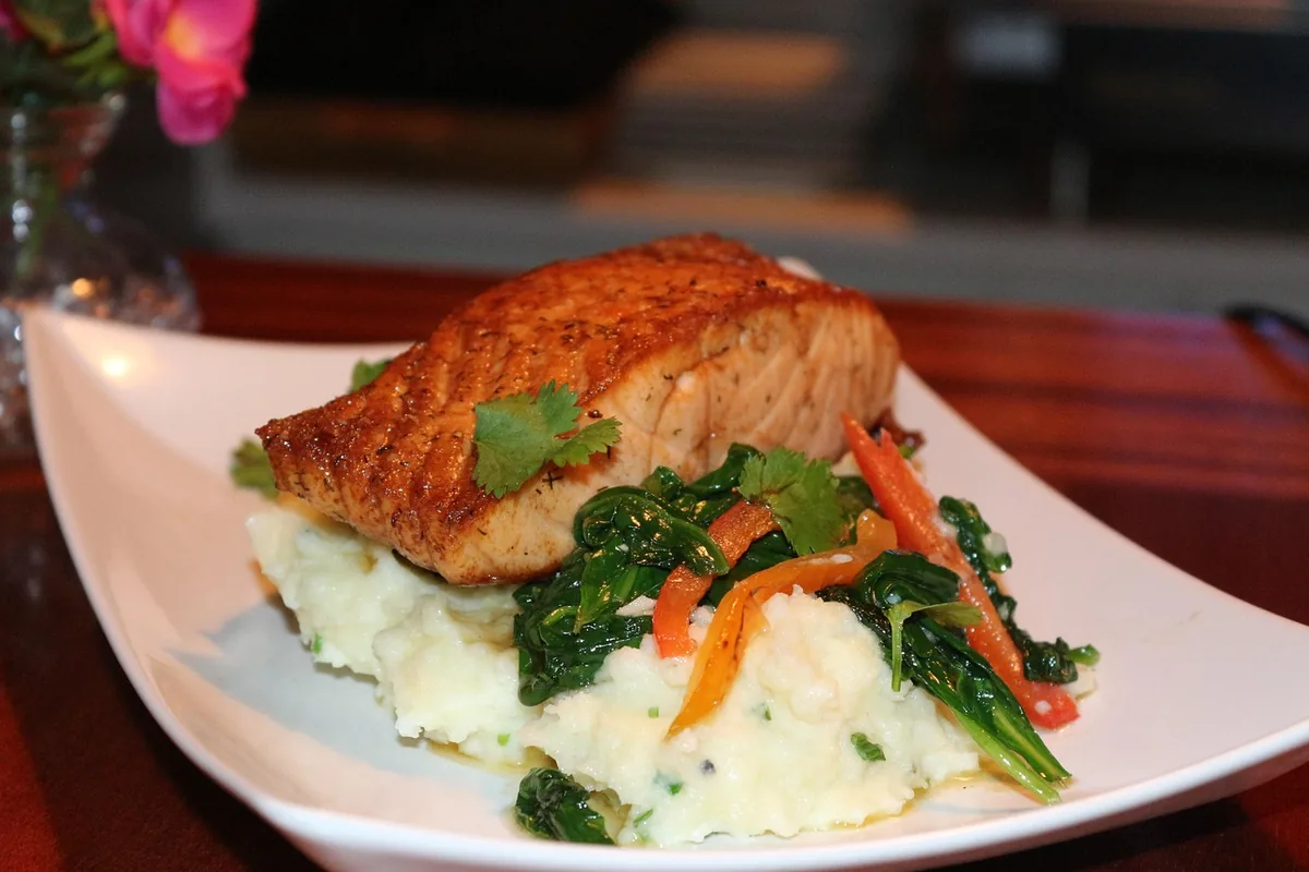 Golden baked salmon fillet on mashed potatoes with sautéed spinach and peppers, served like stuffed salmon