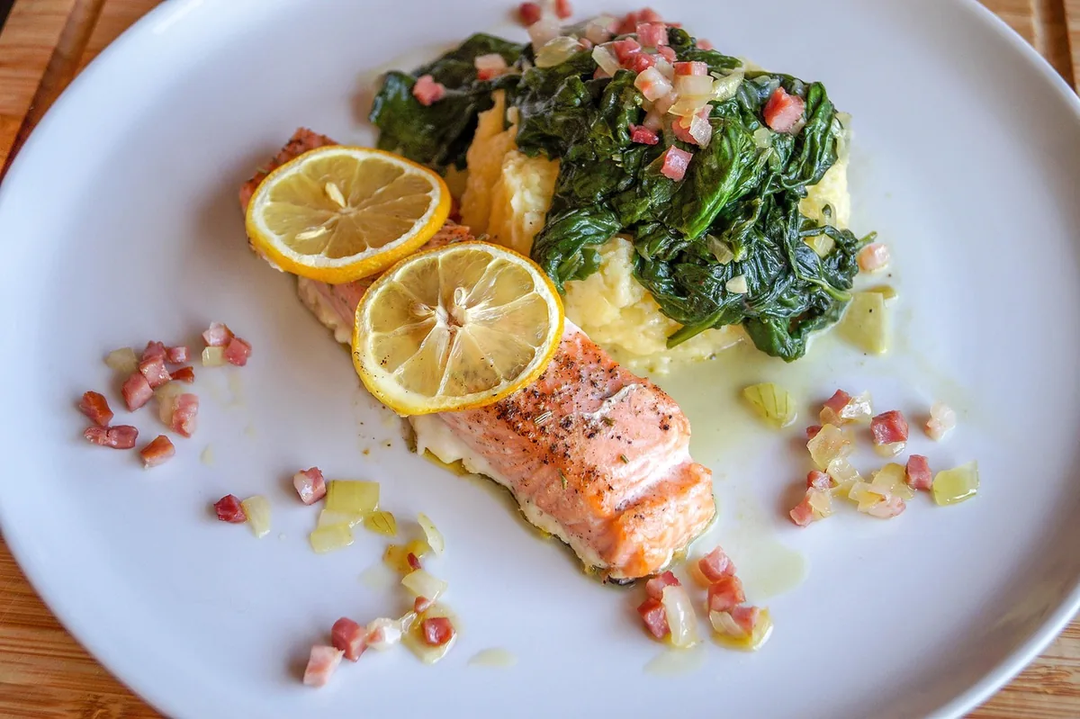 Salmon fillet with creamy spinach and lemon slices on a white plate