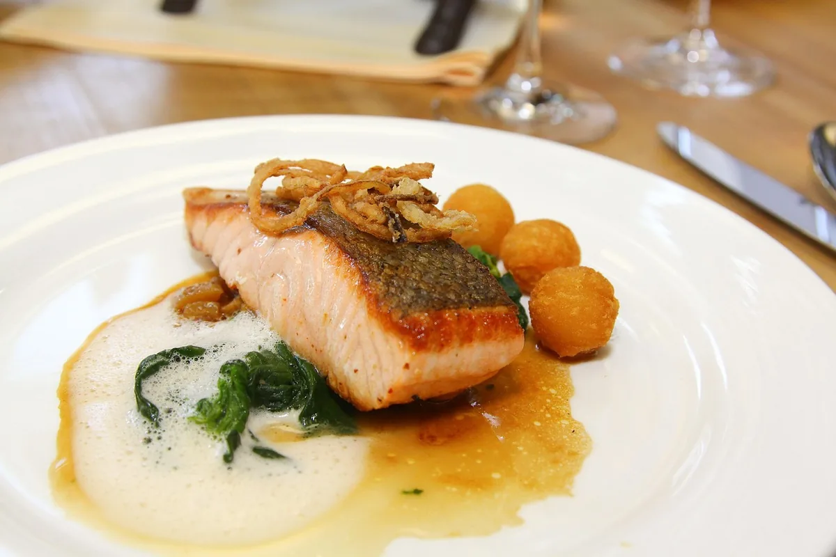 Pan-seared salmon fillet over wilted spinach and a light sauce on a white plate