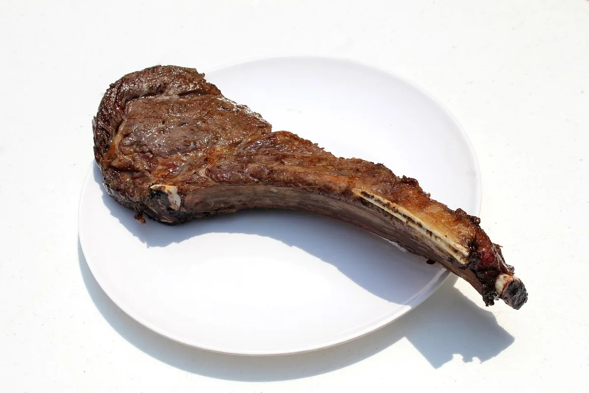 Cooked tomahawk steak with its long frenched bone on a white plate