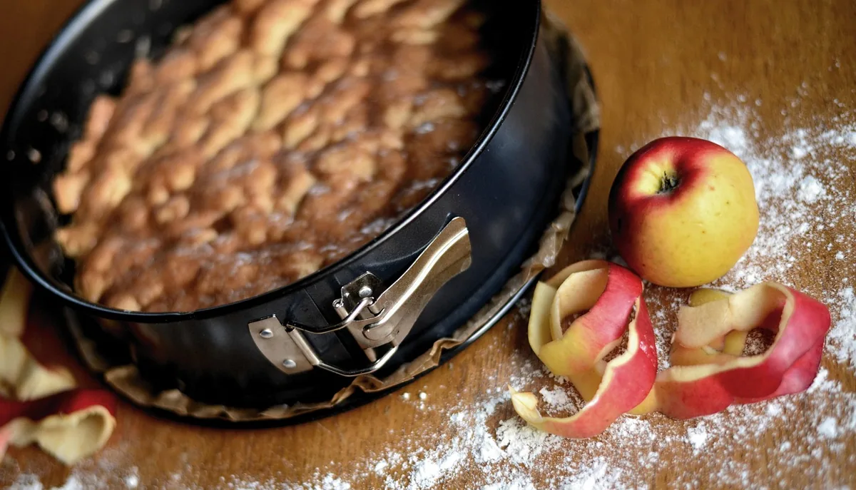 Homemade apple cake in a springform pan with fresh apples and a dusting of flour