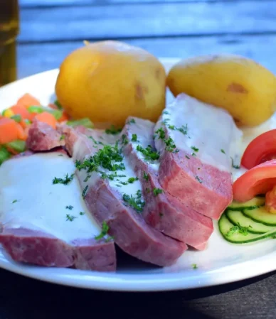 Sliced boiled beef brisket with potatoes, peas and carrots on a plate, like corned beef from the crock pot