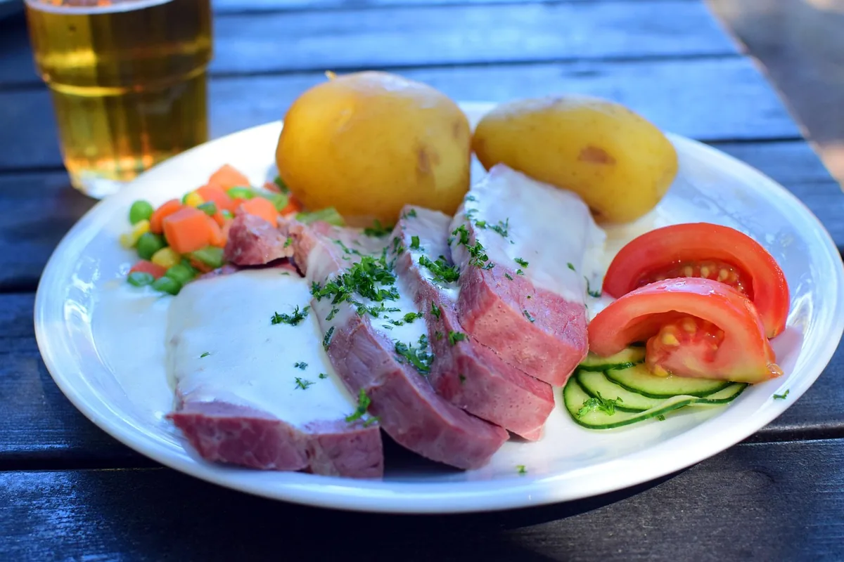 Sliced boiled beef brisket with potatoes, peas and carrots on a plate, like corned beef from the crock pot