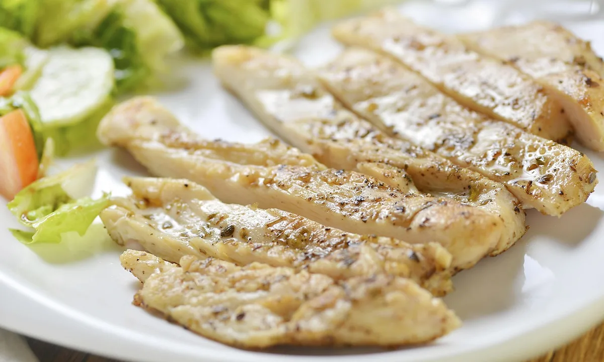 Sliced juicy grilled chicken breast with salad on a white plate