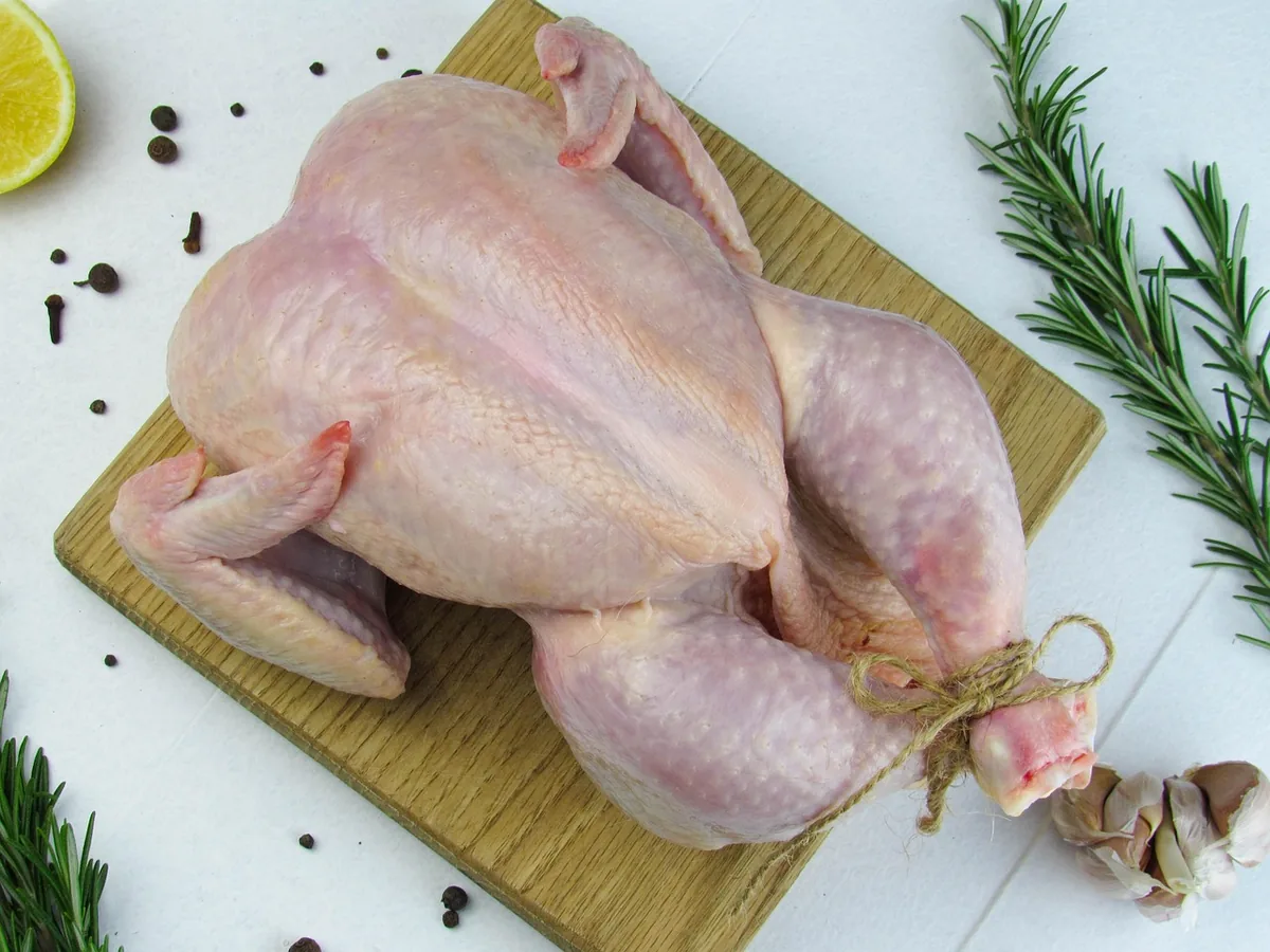 Whole raw chicken on a cutting board with rosemary and garlic, ready to brine