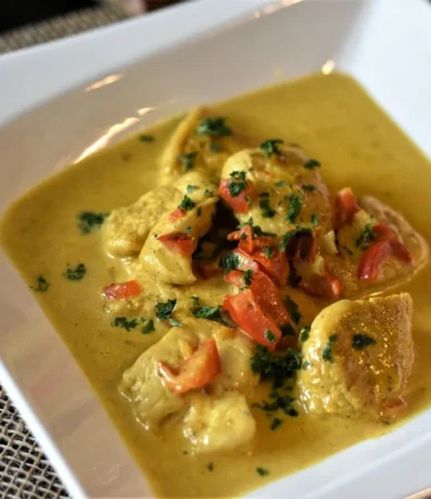 Pieces of chicken in a creamy golden sauce with herbs in a white dish, like chicken stroganoff
