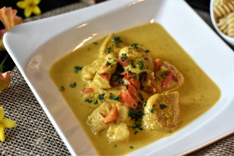 Pieces of chicken in a creamy golden sauce with herbs in a white dish, like chicken stroganoff