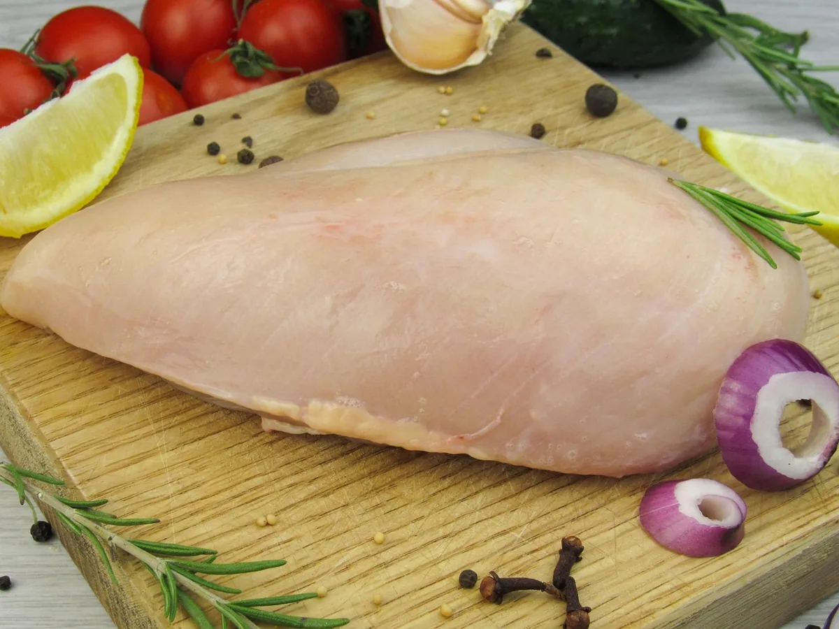 Raw chicken breast on a wooden board with rosemary and red onion, ready to slice for chicken stroganoff