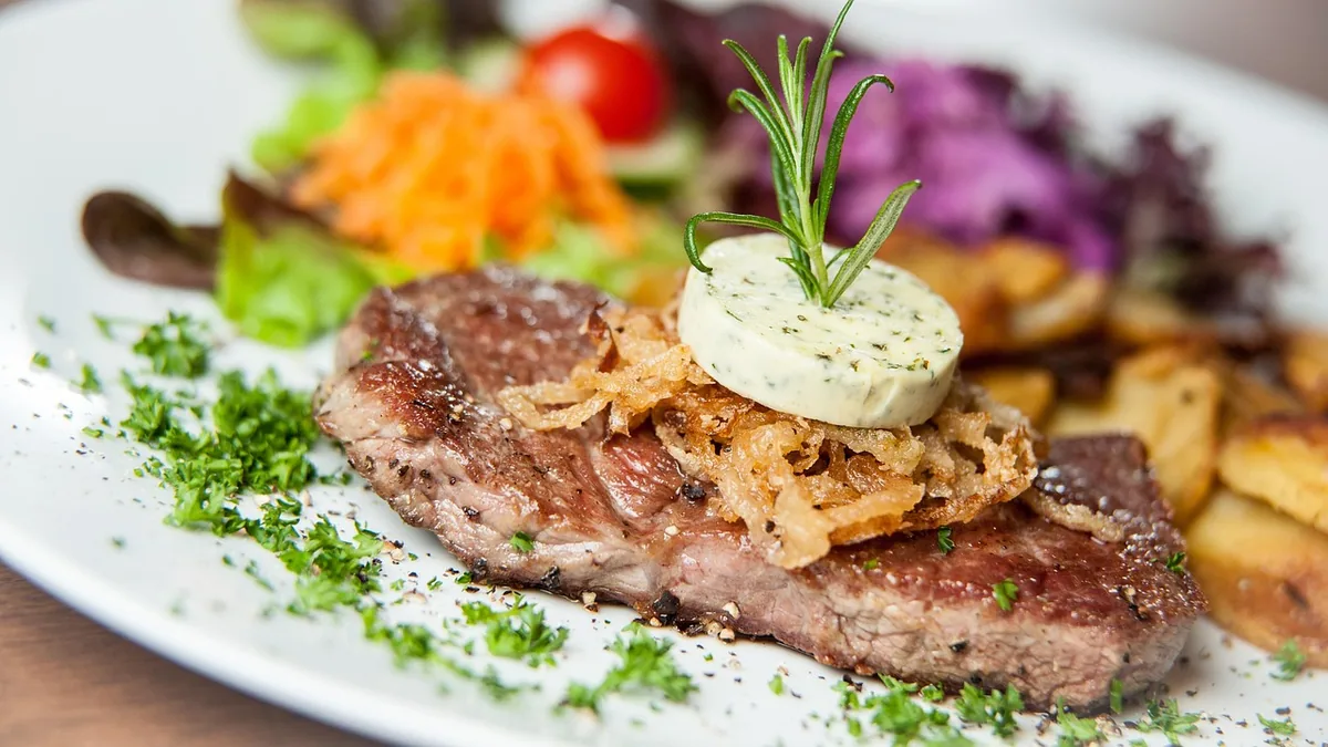 Pan-seared steak topped with herb butter and fried onions, served with roasted potatoes and salad