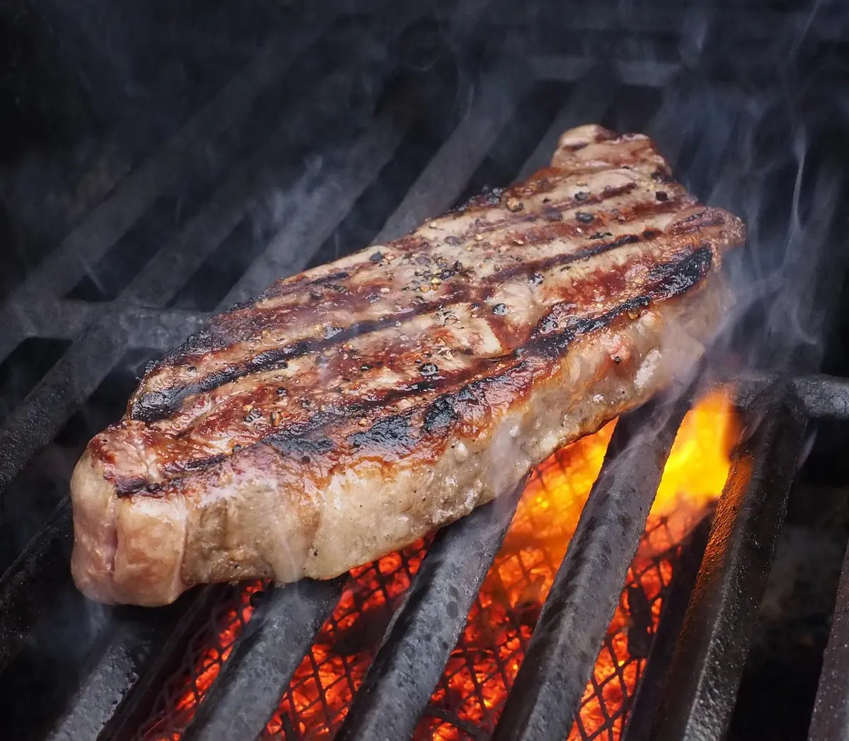 Lean sirloin steak searing on a hot grill grate over flames