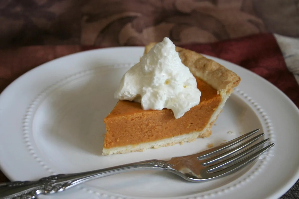 Slice of pumpkin dessert topped with whipped cream on a white plate