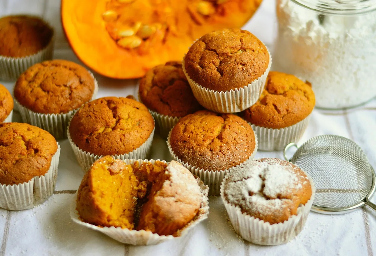 Pumpkin muffins on a table next to a cut pumpkin and a jar of flour