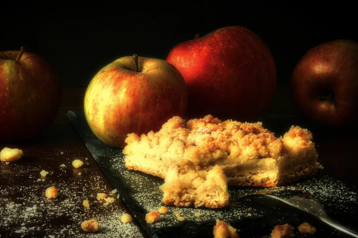 Squares of crumb-topped apple cake next to fresh red apples