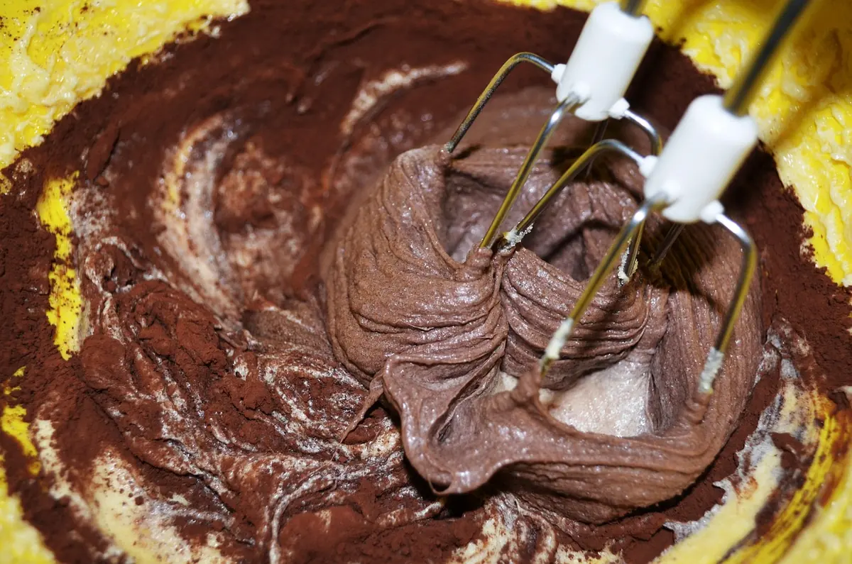 Chocolate frosting being beaten until smooth with a hand mixer in a bowl