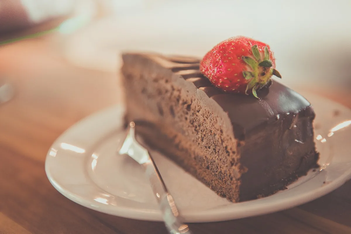 Slice of chocolate cake with glossy chocolate topping and a fresh strawberry on a plate