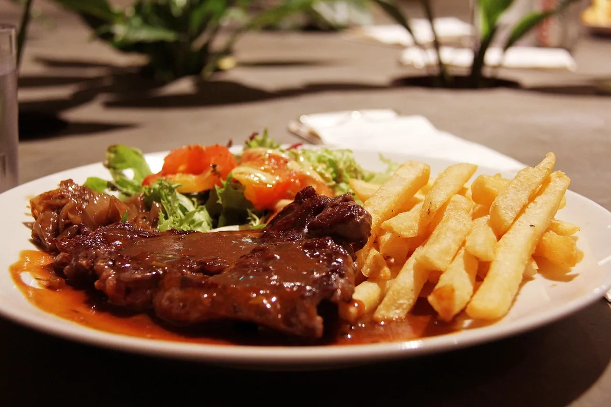 Braised beef steak covered in brown gravy with fries and salad