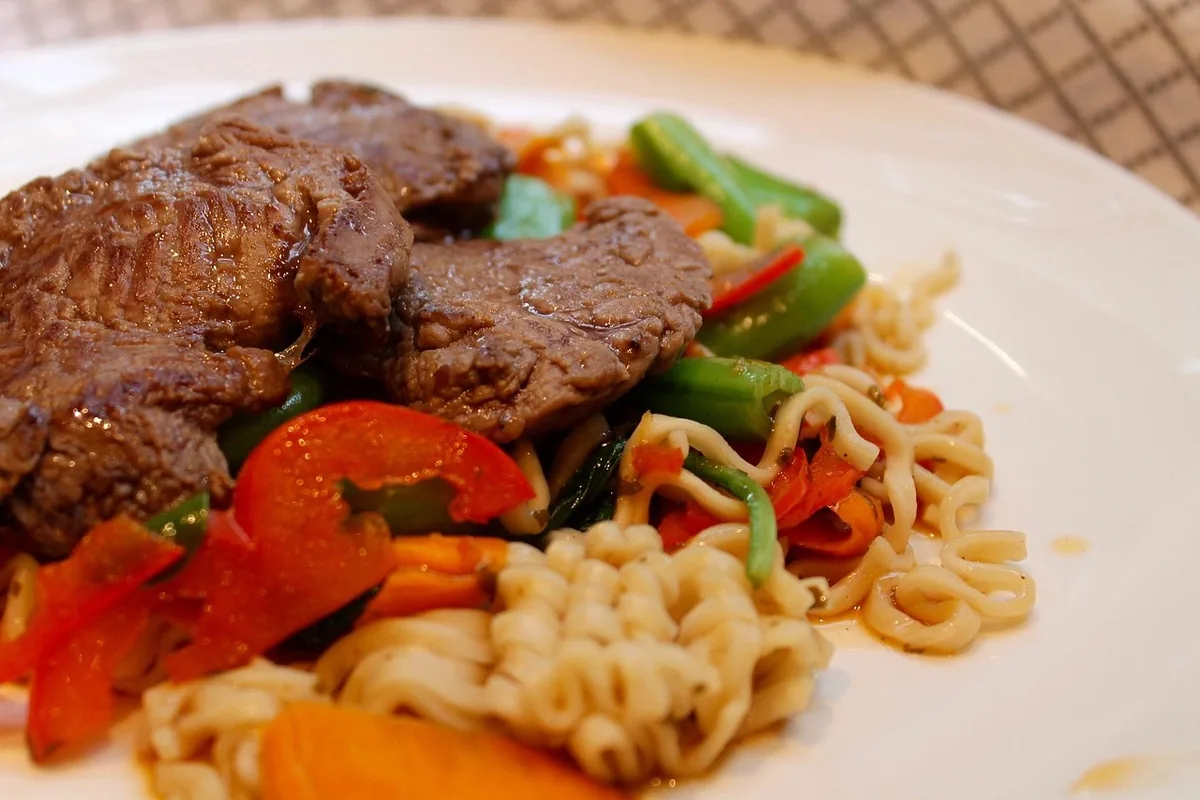Beef slices with red peppers, green beans and noodles on a plate