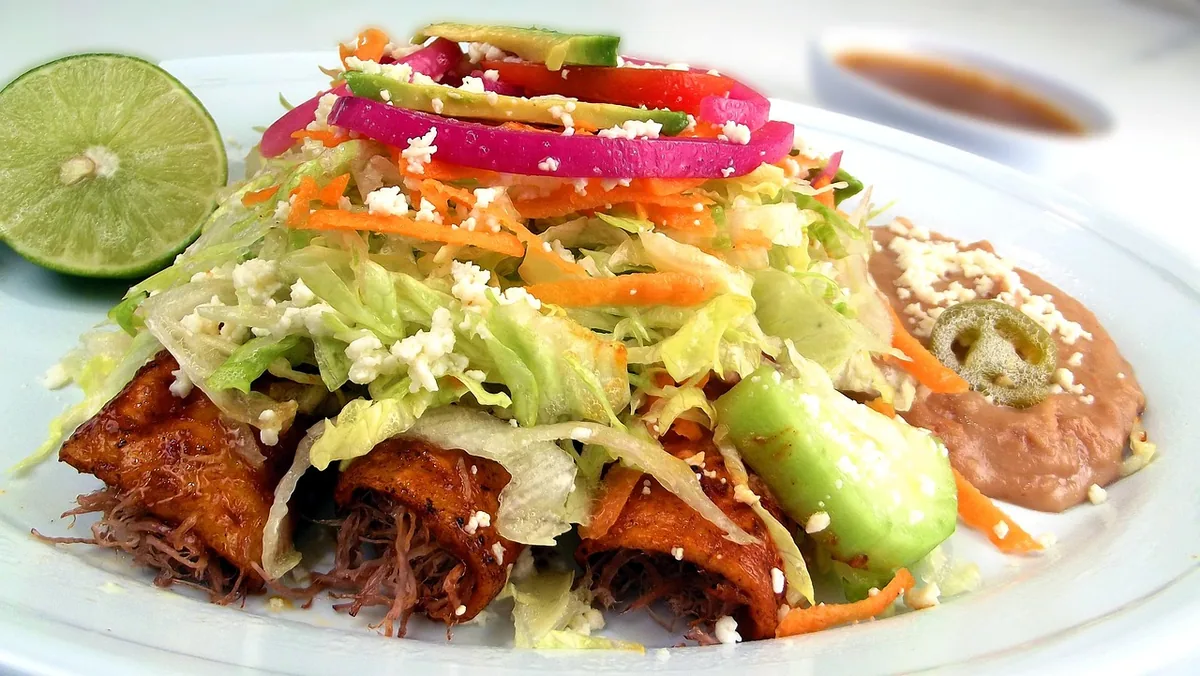 Red enchiladas topped with lettuce, onion, avocado and cheese, served with beans and lime