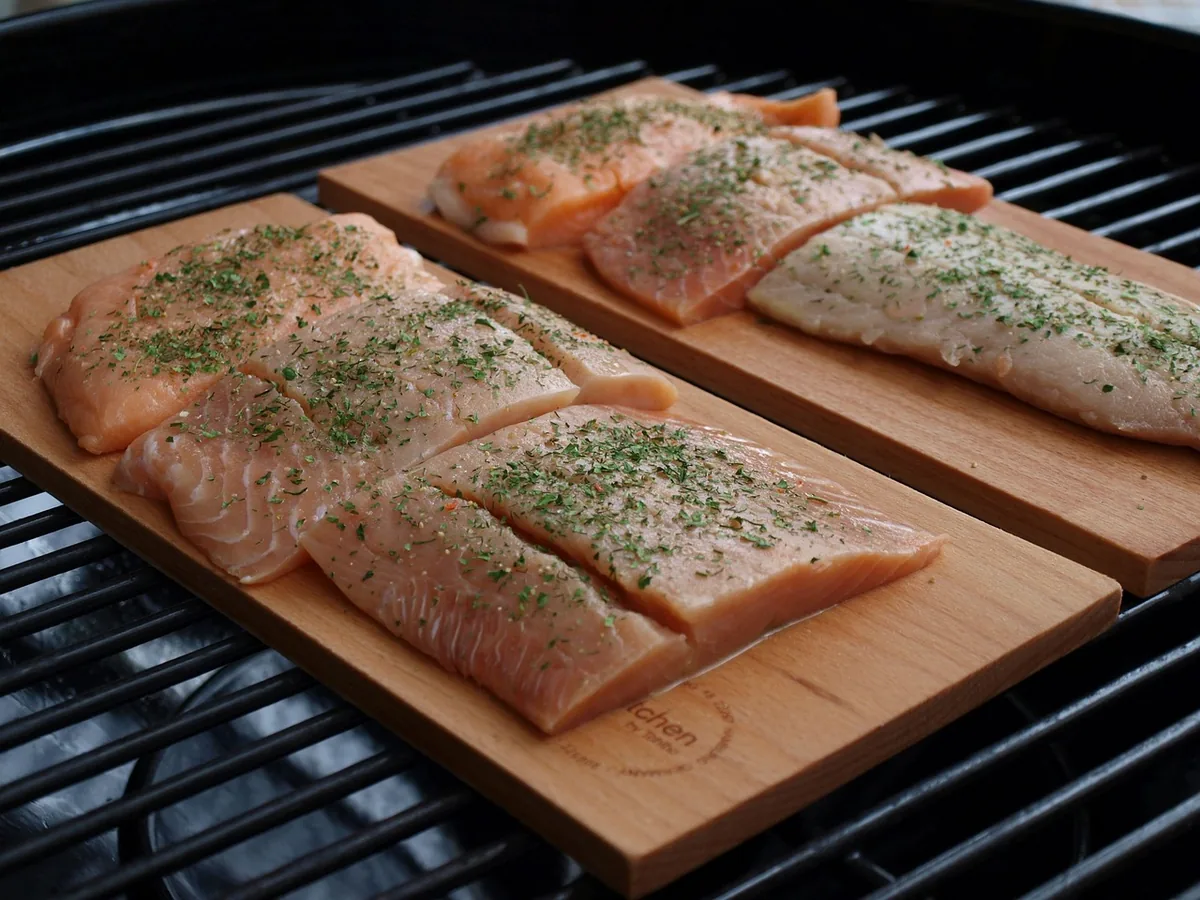 Herb-topped salmon fillets on two cedar planks on a grill